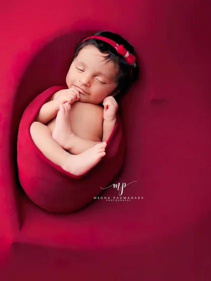 This top-down view shows the baby nestled inside a heart-shaped prop, wrapped in a bold red swaddle. It's a simple, powerful, and love-filled image.