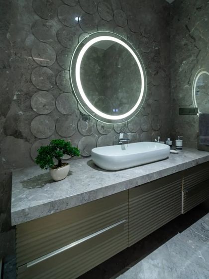 A contemporary bathroom with a textured grey circular-patterned wall, a sleek countertop with an integrated sink, and a large, ring-lit mirror that provides perfect, even lighting.