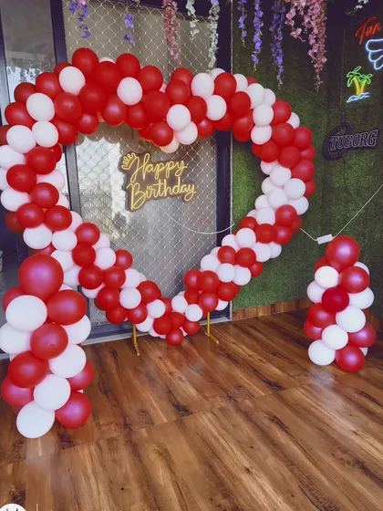 A heart-shaped balloon arch is a classic choice for a romantic photo backdrop. This indoor setup uses red and white balloons and a 'Happy Birthday' sign, creating a perfect frame for pictures.