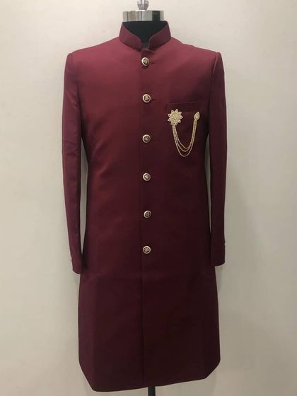 A deep maroon Indo-Western sherwani featuring a stylish gold brooch. This is a modern take on traditional groomswear, tailored for a perfect fit.