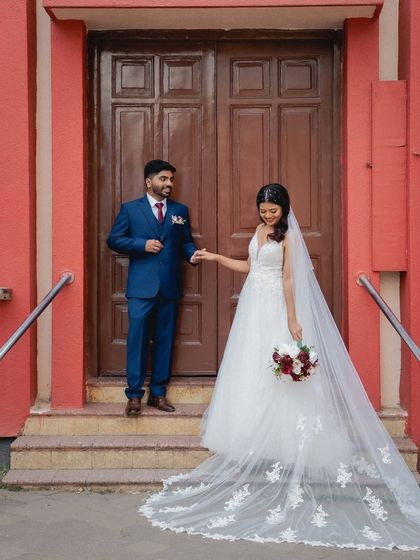 A full-length shot showcasing the bride's magnificent long veil. The couple stands on the steps of the church, creating a grand and timeless image.