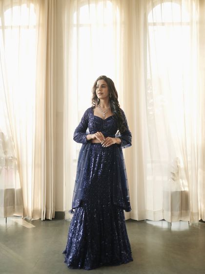 Another full-length shot of the blue sequin lehenga, captured against elegant sheer curtains to create a soft, dreamy effect.