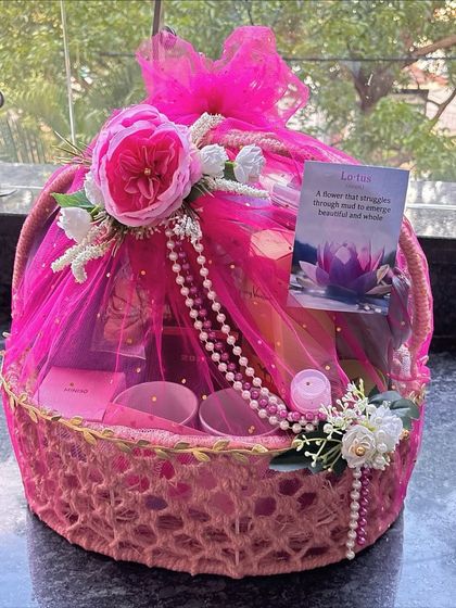 An elegant pink-themed hamper wrapped in beautiful netting. This basket is filled with everyday essentials and adorned with a large pink peony and pearl details.