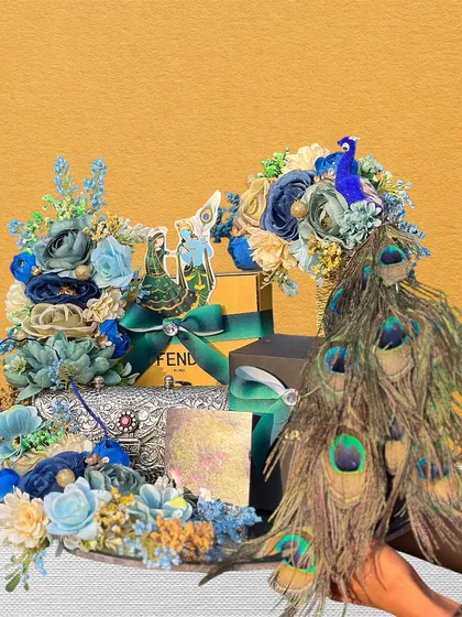 This Teej hamper, held in hand, shows a beautiful arrangement of blue flowers and peacock feathers around gifts from Fendi. It's a great example of how we blend luxury brands with traditional festive decor.