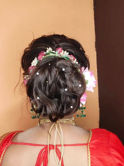 A messy bun hairstyle adorned with a mix of pink and white flowers and pearl pins, perfect for a romantic engagement or reception look.