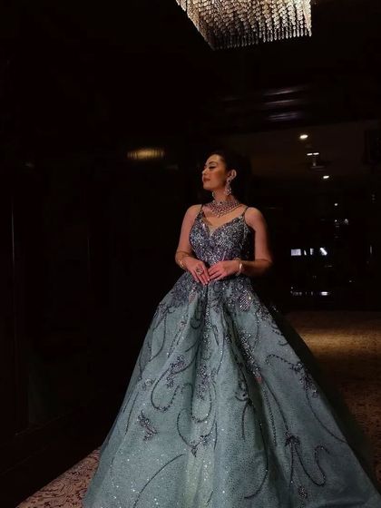 A dramatic shot of a client in a grey-green ball gown in a dimly lit hallway. The sparkle of the dress stands out beautifully.