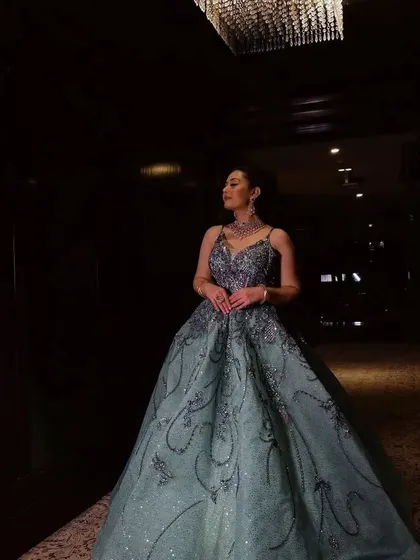 A dramatic shot of a client in a grey-green ball gown in a dimly lit hallway. The sparkle of the dress stands out beautifully.
