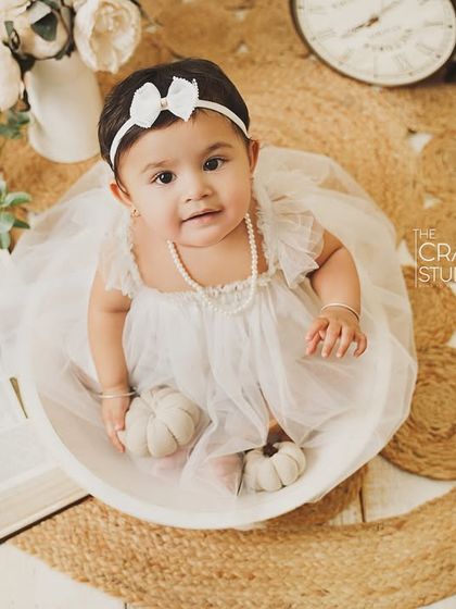 An overhead shot of the birthday girl in her white bowl, looking up with a sweet expression. The neutral props create a soft and gentle mood.