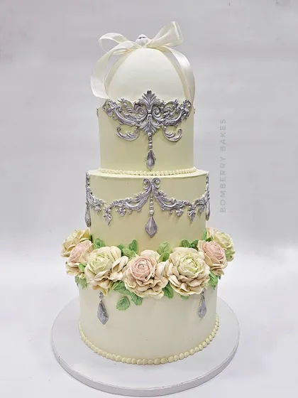 This vintage-style engagement cake features a unique, fully edible ring holder on top, perfect for a surprise proposal. The design combines delicate buttercream piping with beautiful pastel flowers for a timeless look.
