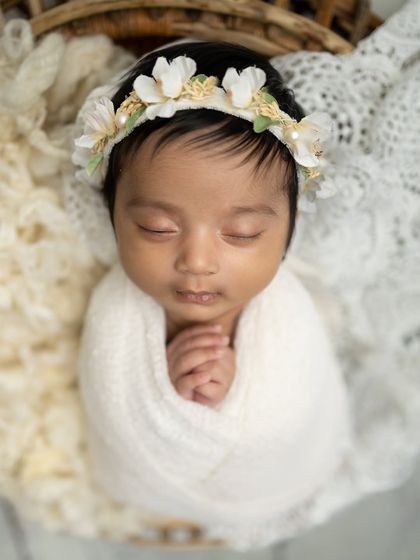 A close-up shot focusing on the baby's serene face and the beautiful details of the floral headband.