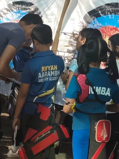 Archers and coaches gather around the target to score the arrows during the U-10 trials.