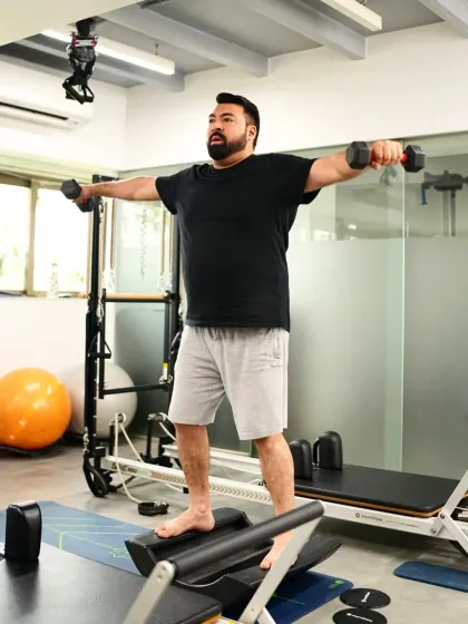 A client works on his balance and shoulder strength using dumbbells on a rocker board. This exercise forces the small stabilizing muscles to fire, improving coordination and preventing injury.