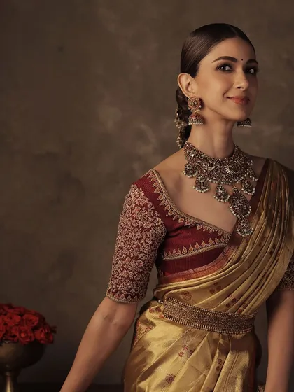 Another view of the deep red embroidered blouse and gold saree, showcasing the beautiful drape of the silk and the detailed craftsmanship of the blouse.