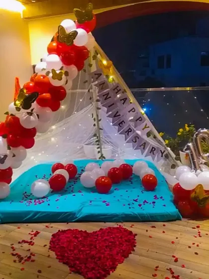 This is a 10th anniversary tent setup, featuring red and white balloons with butterfly details. A heart made of rose petals on the floor adds a romantic touch to this intimate celebration space.