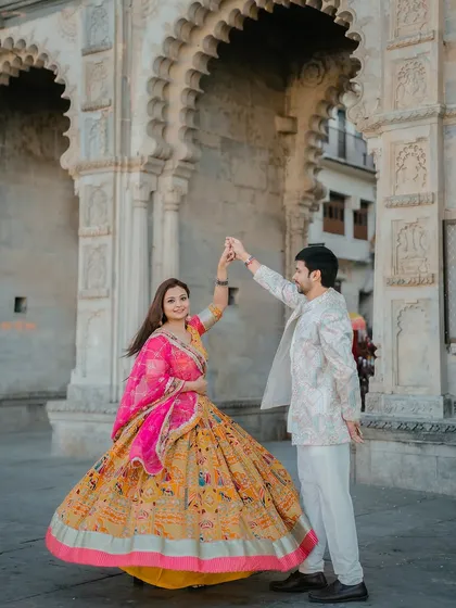 A joyful moment as the couple twirls, showcasing the beautiful flare of the bride's colorful lehenga against the historic architecture.