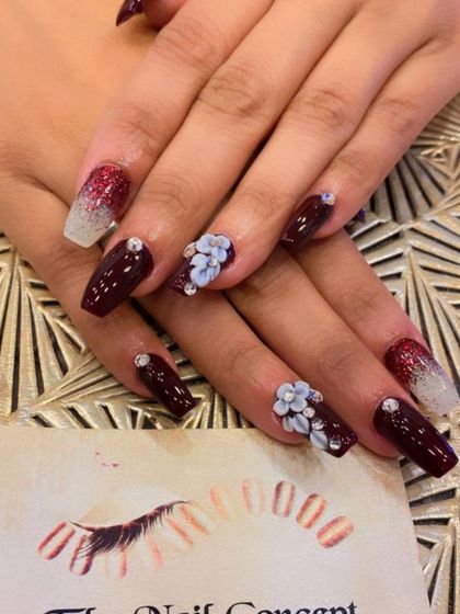 A sophisticated design combining deep maroon nails with ombre glitter and 3D floral art. The sculpted white flowers are accented with tiny silver beads for a detailed, textured look.