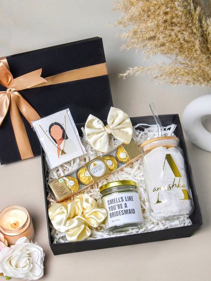 A high-angle shot of a bridesmaid proposal box. The elegant black and gold theme, combined with items like a custom candle and chocolates, creates a luxurious and inviting image.