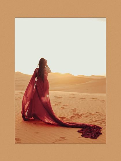 A solo portrait of the bride-to-be against the setting sun in the desert. The light catching her flowing red gown creates a breathtaking and ethereal effect.