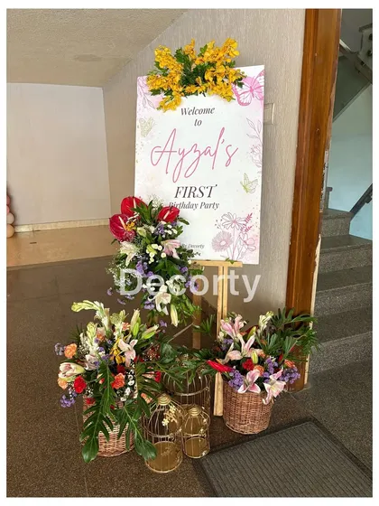 A beautiful welcome easel for a butterfly-themed party, decorated with fresh, colorful flowers.