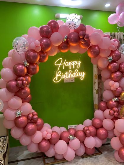A beautiful circular balloon arch in shades of pink and rose gold, with a 'Happy Birthday' neon sign. This setup is perfect for a chic and feminine celebration.
