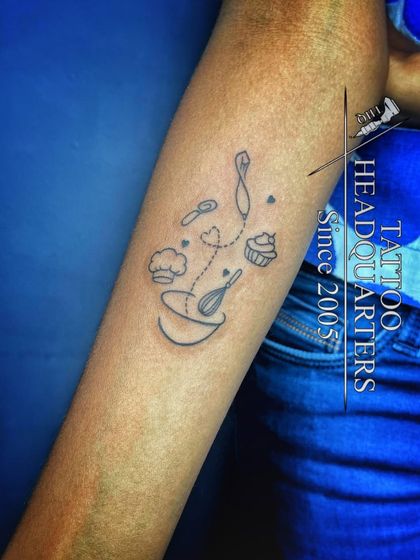 A whimsical tattoo for a baker or chef, featuring a mixing bowl, whisk, and other baking elements floating above.