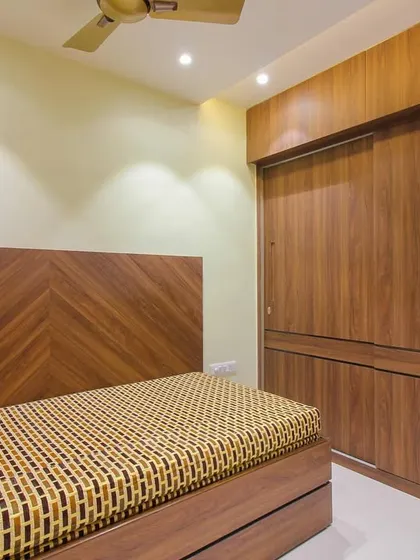 A minimalist bedroom design with a focus on natural textures. The chevron-patterned wooden headboard and matching sliding wardrobe create a warm and cohesive look.