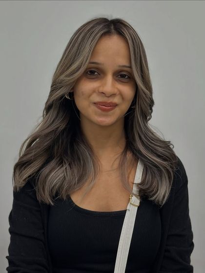 A happy client showing off her new ash hair color. The cool tones and face-framing pieces are perfectly blended.