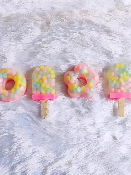 A set of four candy-themed soaps, including donuts and popsicles, on a fluffy white background.