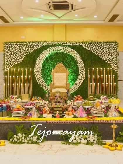 A half-saree ceremony setup with a green backdrop, a floral wreath, and tall candles, creating an elegant and serene atmosphere.
