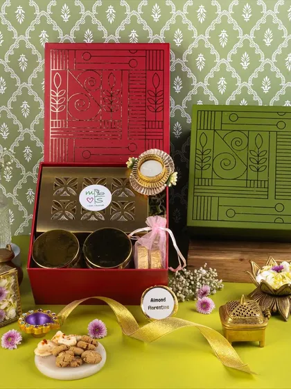 A vibrant and modern take on Diwali gifting. The contrasting red and green boxes, paired with a patterned background and fresh flowers, create a visually exciting and contemporary look.