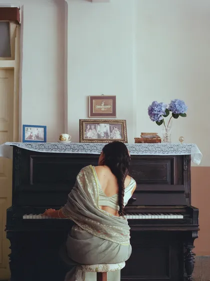 A woman in a mint green saree at a piano in a vintage Bombay home. This scene was styled to feel personal and contemplative, as if we've stumbled upon a private moment.