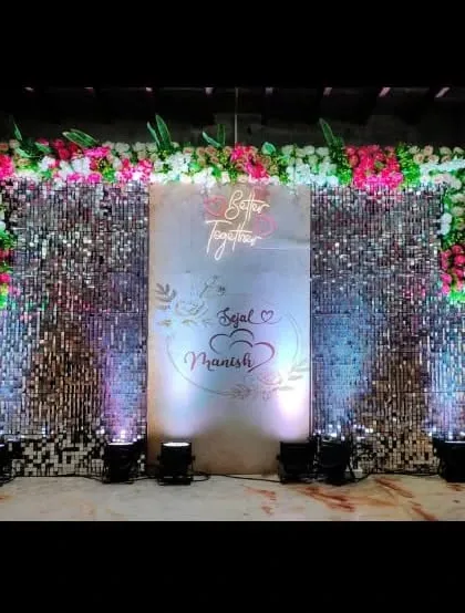A chic and modern sangeet or reception stage featuring a dazzling silver shimmer wall. A custom 'Better Together' neon sign and the couple's names, Sejal and Manish, add a personal touch, perfect for a glamorous party photo booth.