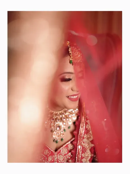 A soft and dreamy close-up of the bride smiling, with her red veil creating a beautiful, artistic blur in the foreground.