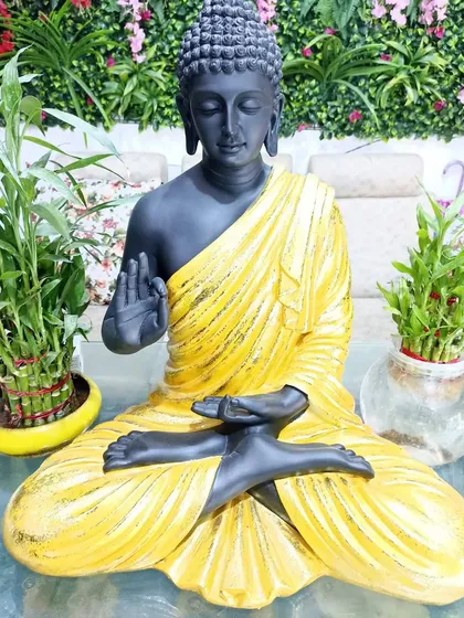 This unique Buddha statue features a black body with a contrasting yellow robe. It's a modern take on a classic symbol of peace.
