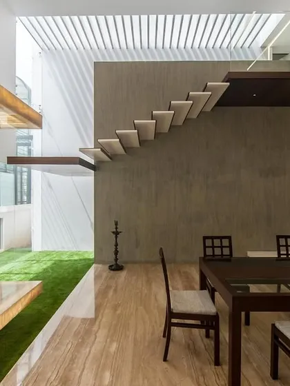 The dining and pooja space in the Sandeep & Neelam residence opens directly onto an indoor grass courtyard, illuminated by a large skylight. This design brings natural light and greenery into the heart of the home.