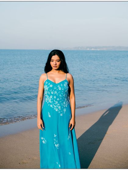 A simple and beautiful full-length portrait against the vastness of the ocean. The composition is clean and focuses on the model.