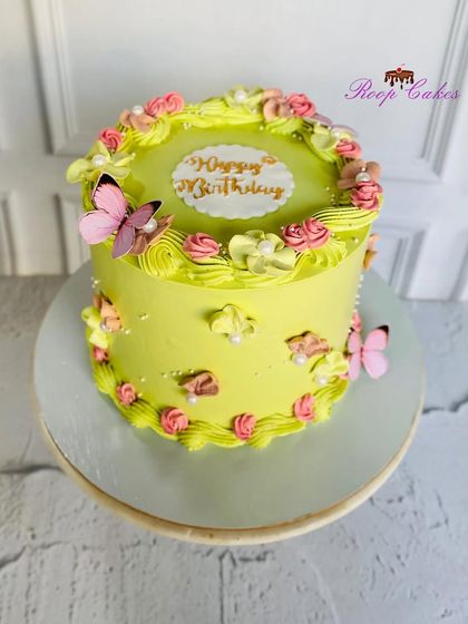 A lovely Rasmalai cake in a vibrant lime green, decorated with pink and yellow rosettes and butterflies.