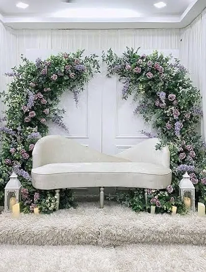 For a touch of classic elegance, we designed this stunning backdrop featuring a white chaise lounge set against a dramatic arch of purple flowers and greenery. The lanterns and candles add a soft, romantic glow.