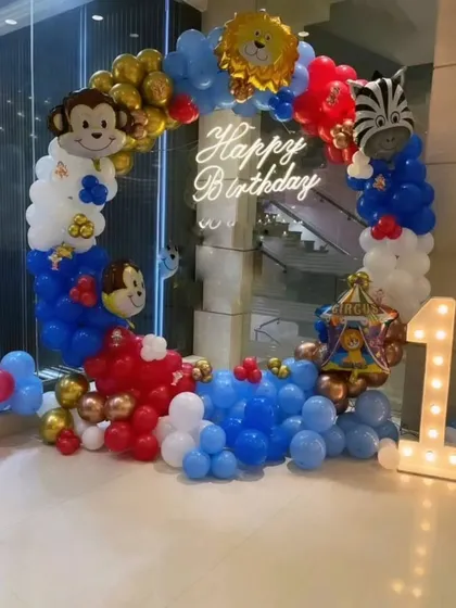 A playful circus and jungle animal theme for a first birthday. This circular balloon arch is decorated with monkey, lion, and zebra foil balloons, along with a light-up number "1" and a neon sign.