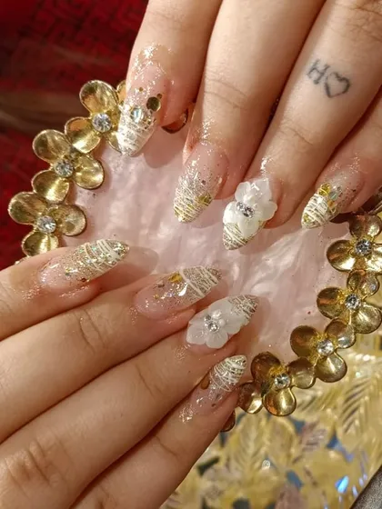 An ethereal design featuring gold thread work, gold flakes, and 3D white floral accents on long, clear extensions.