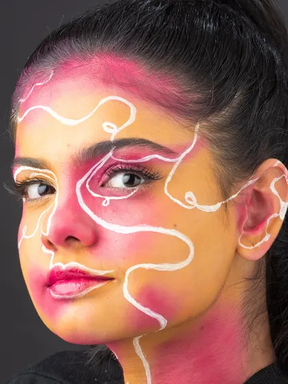 A vibrant face paint look with a pink and orange base and abstract white line work, demonstrating skills in avant-garde makeup.