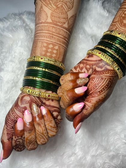 A beautiful temporary extension set for a bride, featuring a soft pink and white ombré effect. The look is elevated with a full gold glitter accent nail, perfectly complementing her green bangles and detailed mehndi design.