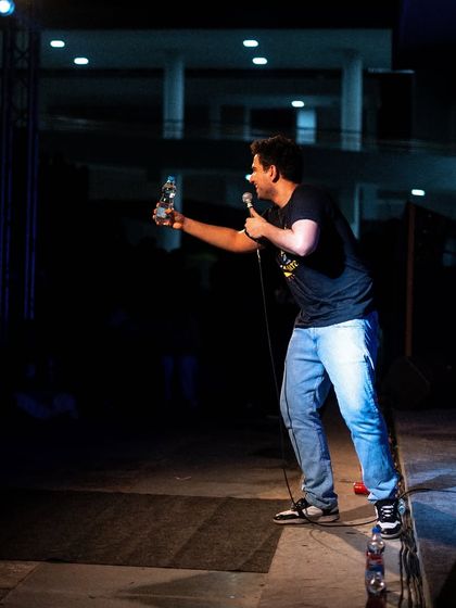 Samay Raina holding up a bottle of water, a signature part of his on-stage persona, during his show at Dhruva, IIM Trichy.