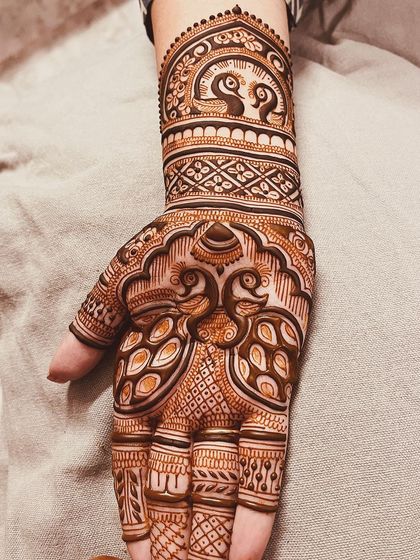 A beautiful traditional peacock design on the back of the hand, with delicate patterns extending up the wrist.