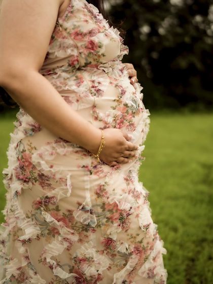 A close-up on the texture of the floral dress against the baby bump, a beautiful detail shot that celebrates both fashion and pregnancy.