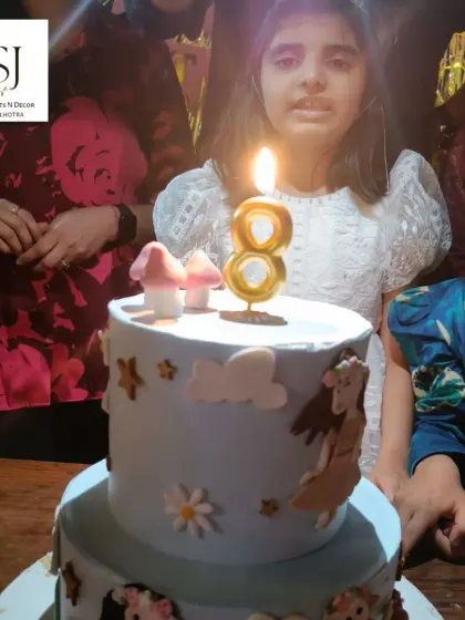 The birthday girl at the fairy-themed party, about to cut her beautiful two-tiered cake decorated with fairy and mushroom elements.