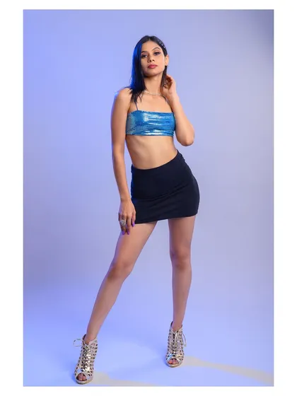 A full-length shot of a model in a metallic blue top and black skirt. The cool-toned lighting complements the outfit and creates a trendy, futuristic vibe.