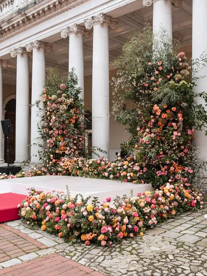 A closer look at the mandap, which is overflowing with a lush arrangement of pink, peach, and orange roses. The organic, garden-style floral design contrasts beautifully with the formal architecture.