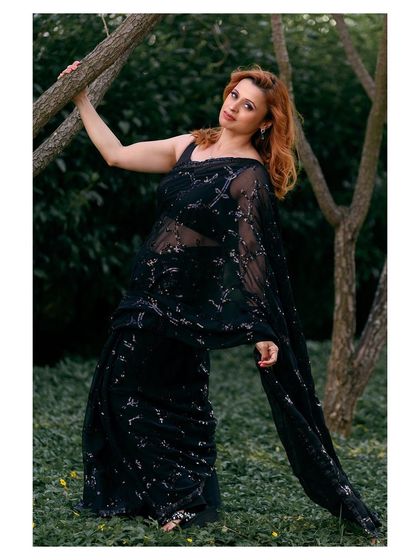 An outdoor shoot for a black sequined saree. The natural, green background provides a beautiful contrast to the dark, glamorous fabric.