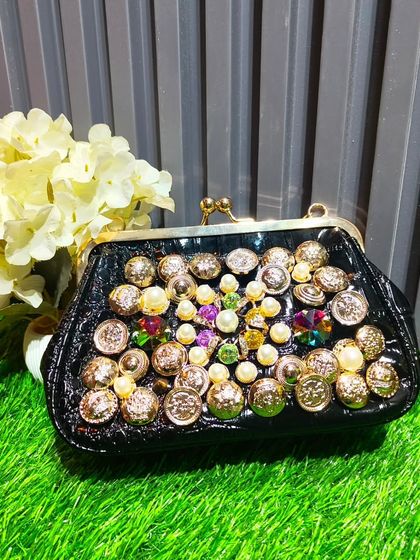 For a bold and eclectic look, this black clutch is adorned with a variety of colorful gems, pearls, and vintage-style buttons.